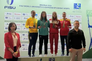Vier Medaillengewinnerinnen stehen bei einer Siegerehrung auf dem Podest vor einer FISU-Rückwand und halten ihre Medaillen. Zwei weitere Personen stehen vor dem Podest.