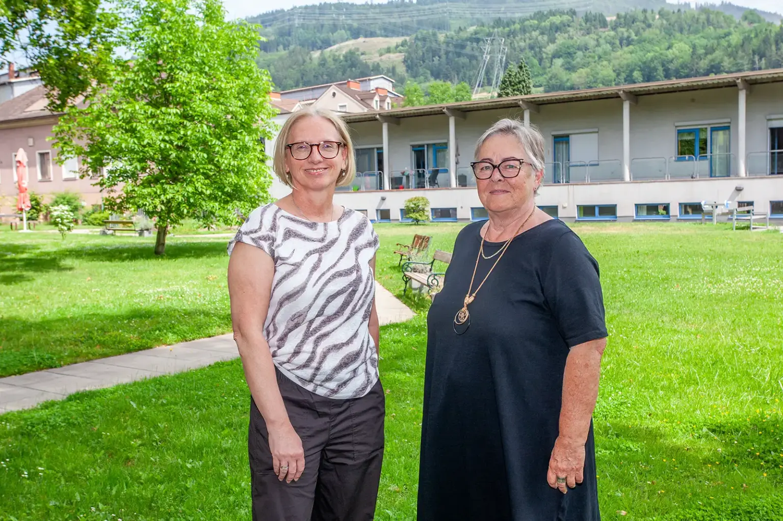 Zwei Frauen stehen auf einer Grünfläche vor einem Haus