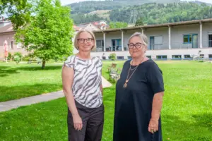 Zwei Frauen stehen auf einer Grünfläche vor einem Haus