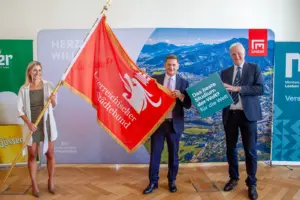 Eine Frau und zwei Männer halten eine Flagge und einen würfelförmigen Karton