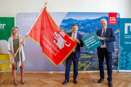 Eine Frau und zwei Männer halten eine Flagge und einen würfelförmigen Karton
