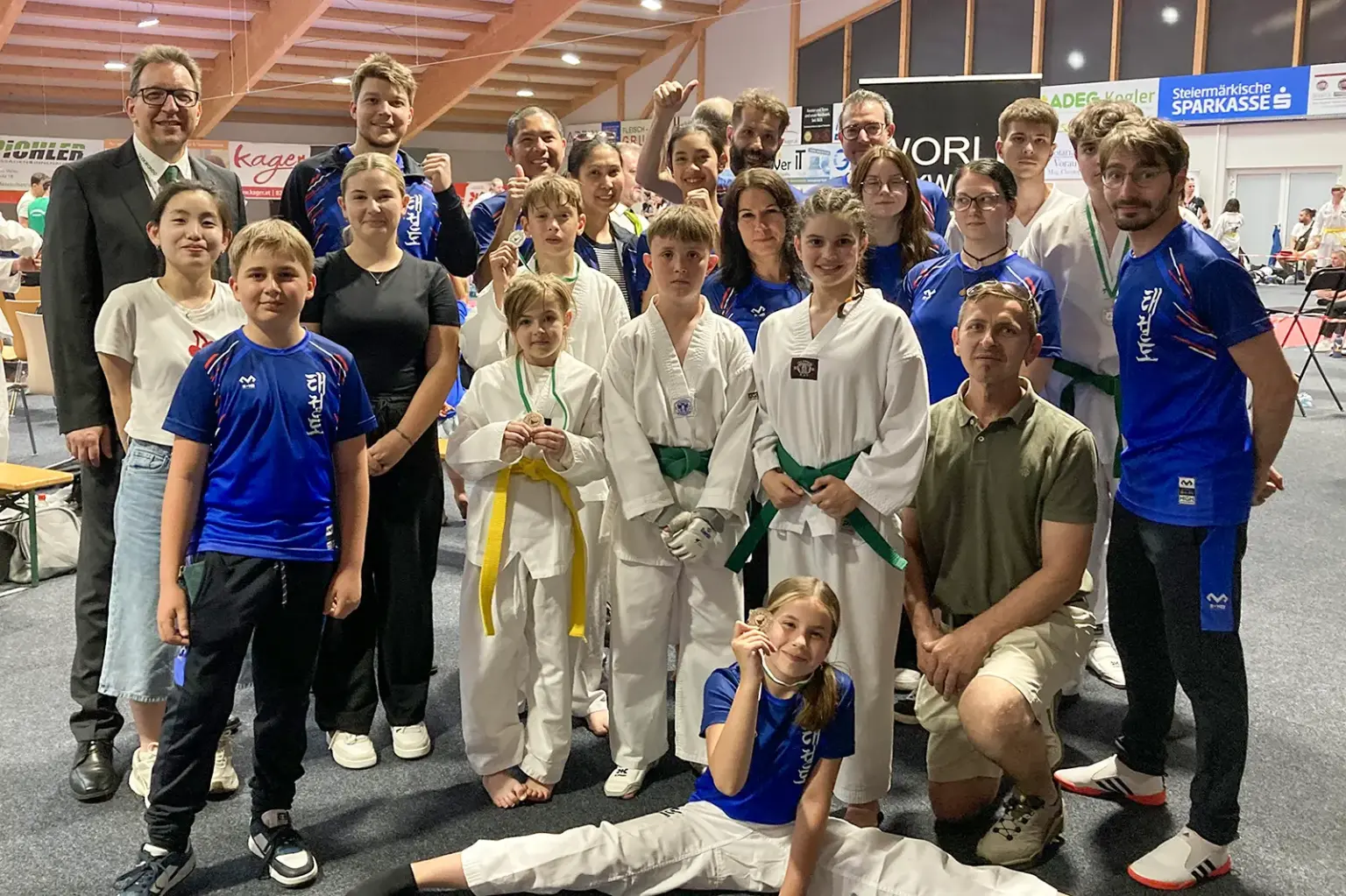Premiere für Leobener Taekwondo Club Mitglieder eines Taekwondo-Vereins präsentieren sich nach einem Turnier für ein Gruppenfoto in einer Sporthalle. Kinder, Jugendliche und Erwachsene in Trainingskleidung und Kampfanzügen zeigen Medaillen und posieren gemeinsam mit ihren Betreuern.