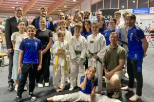 Mitglieder eines Taekwondo-Vereins präsentieren sich nach einem Turnier für ein Gruppenfoto in einer Sporthalle. Kinder, Jugendliche und Erwachsene in Trainingskleidung und Kampfanzügen zeigen Medaillen und posieren gemeinsam mit ihren Betreuern.