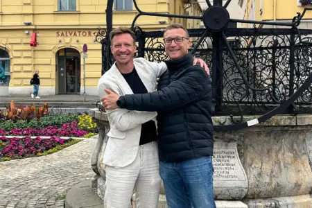 Neuer Trainer beim SC Bruck Zwei Männer stehen gut gelaunt vor einem kunstvoll geschmiedeten Brunnen in einer Innenstadt und umarmen sich freundschaftlich.
