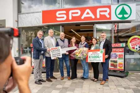 Neuer Sparmarkt in Mürzzuschlag offiziell eröffnet Eine Gruppe von Personen steht mit einem großen Schlüssel und einem Spendenscheck vor einem Geschäftslokal