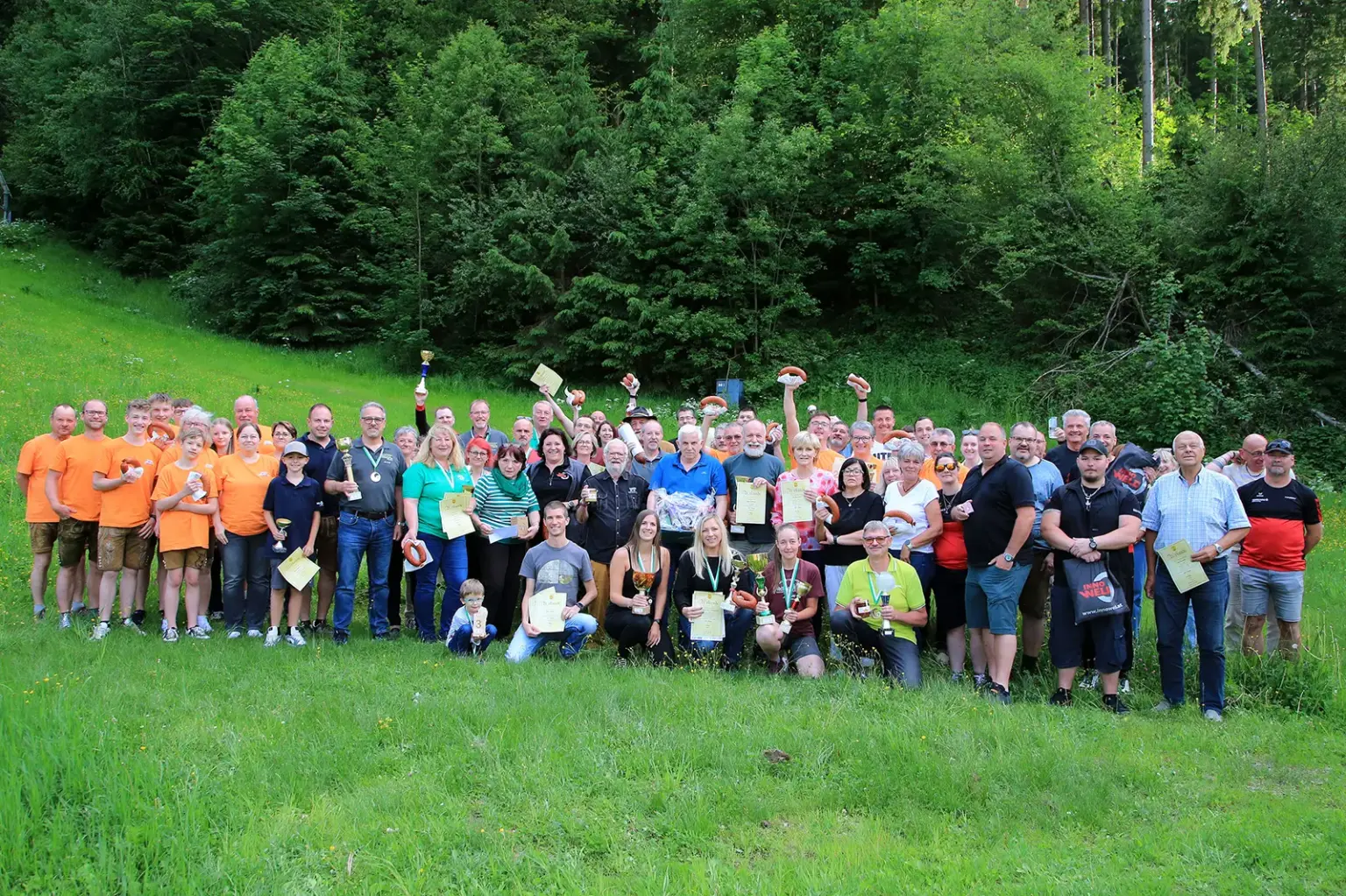 Zahlreiche Teilnehmerinnen und Teilnehmer versammeln sich auf einer Wiese vor einem Waldstück für ein Gruppenfoto.