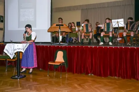 Geschichte der Veitscher Höfe Eine Frau im Dirndl spricht vor einer Bühne mit Musikern in ein Mikrofon