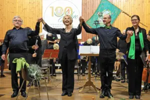 Zwei Frauen und zwei Männer halten sich vor einer Gruppe Musikern an den Händen