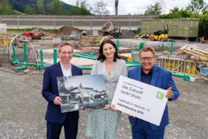 Eine Frau und zwei Männer mit zwei Tafeln. Eine zeigt ein Bild einer E-Tankstelle, die andere Informationen der Energie Steiermark