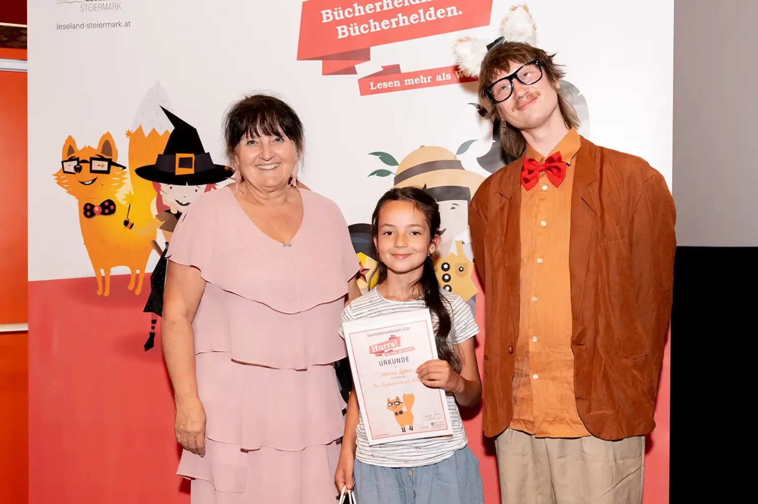 St. Peter-Freienstein: Preisgekrönte Nachwuchsautorin Ein Mädchen mit einer Urkunde zwischen zwei Erwachsenen.