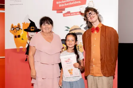 Ein Mädchen mit einer Urkunde zwischen zwei Erwachsenen.