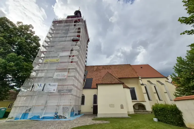 St. Lorenzener Pfarrkirche erstrahlt bald im neuen Glanz Die Kirche von St. Lorenzen mit eingerüstetem Kirchturm während Sanierungsarbeiten. Über dem Gebäude ziehen dunkle Wolken auf.