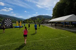 Auf einer weitläufigen Wiese mit Bergkulisse nehmen mehrere Menschen an einer Laufveranstaltung teil.