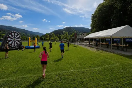 Charitylauf rund um den Stanzer Teich Auf einer weitläufigen Wiese mit Bergkulisse nehmen mehrere Menschen an einer Laufveranstaltung teil.