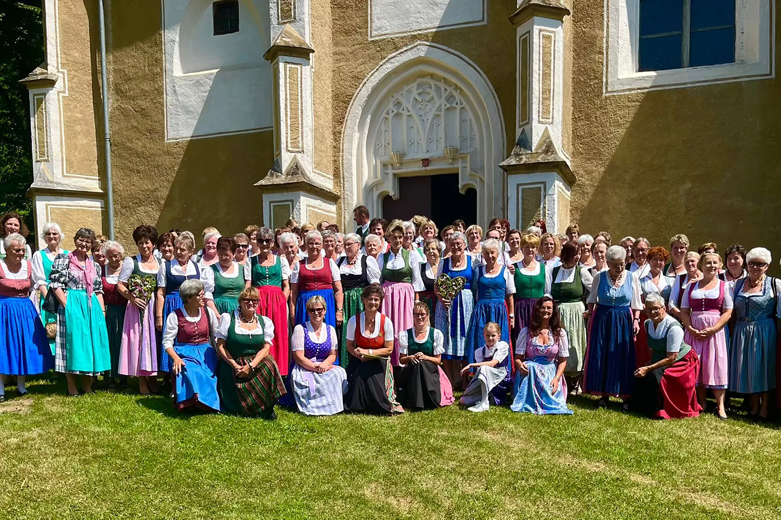 Eine große Gruppe von Frauen in Dirndlkleidern posiert vor einer Kirche