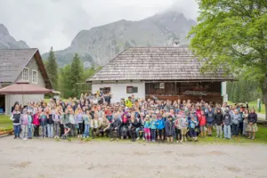 Ein große Gruppe von Personen mit vielen Kindern staht auf einer Wiese vor einem alten Hofgebäude
