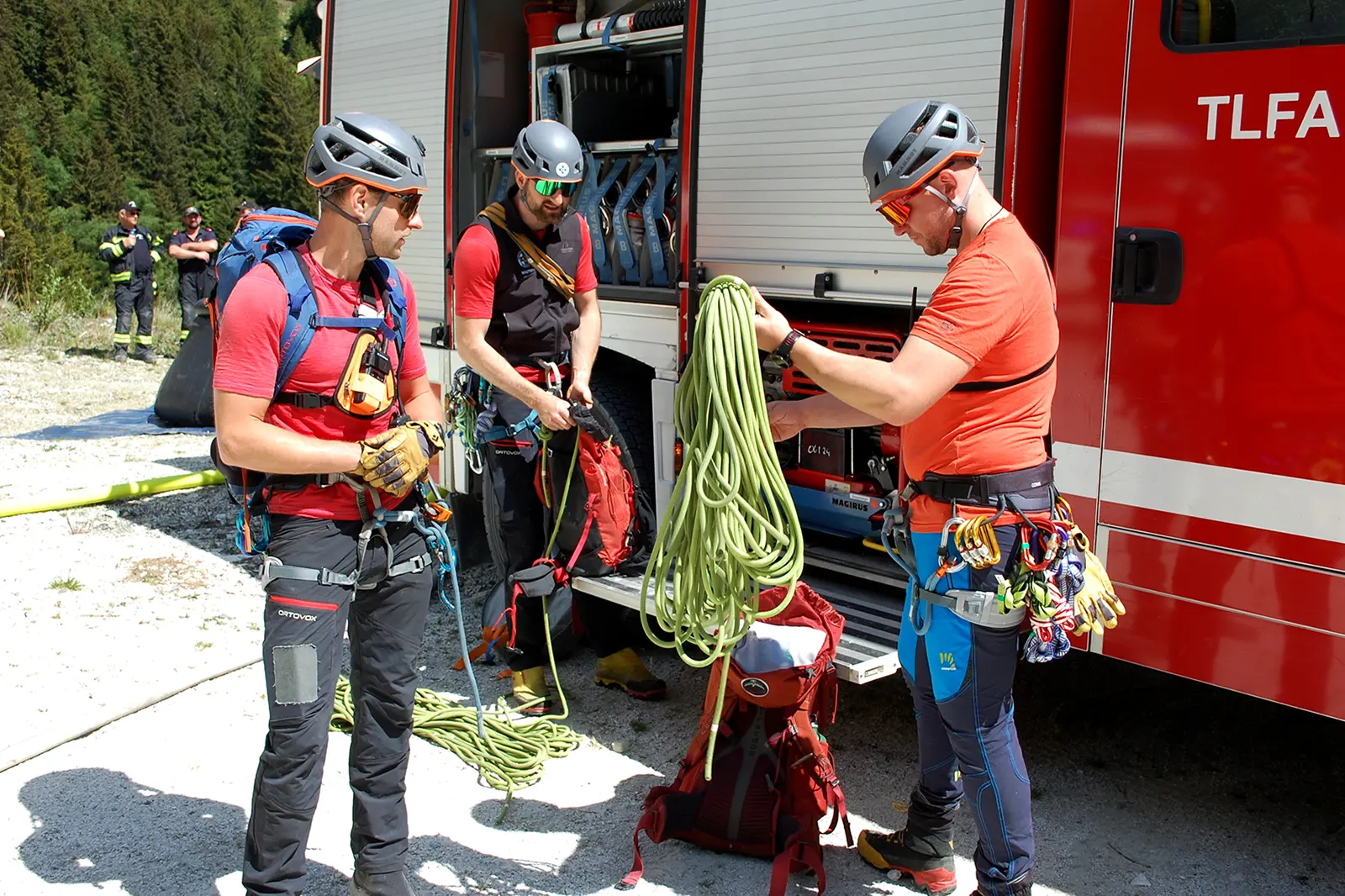 Drei Männer mit Kletterausrüstung vor einem Feuerwehrauto.