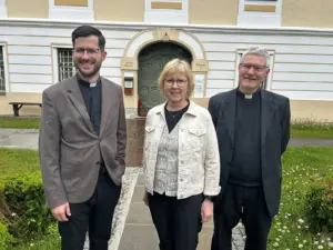 Zwei Priester und eine Frau stehen vor einem hellen Gebäude