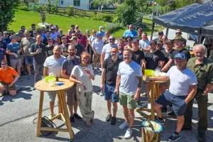 Eine großen Gruppe von Personen steht im Freien rund um zwei kleine Tische