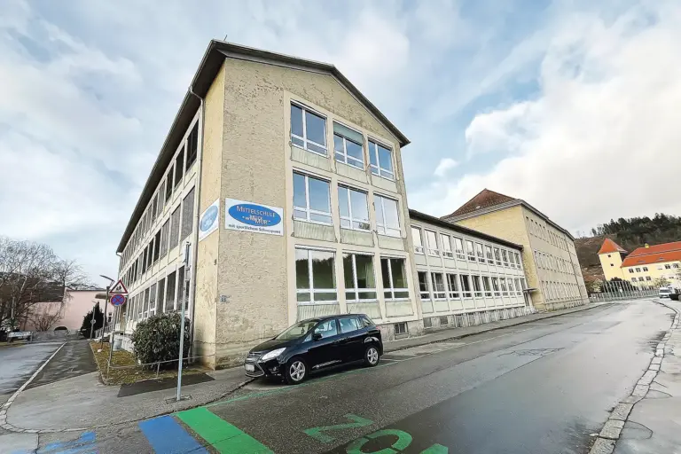 50 Löcher zum Check der Brucker Mittelschule Ein dreigeschoßiges Gebäude, darauf eine Tafel mit der Aufschrift "Mittelschule Bruck an der Mur"