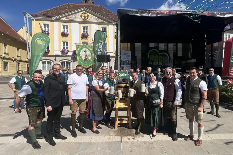 Bruck: Ein Tag voller Brauchtum, Musik und Geselligkeit Eine Gruppe von Personen in Tracht beim Bieranstich auf einem großen Platz