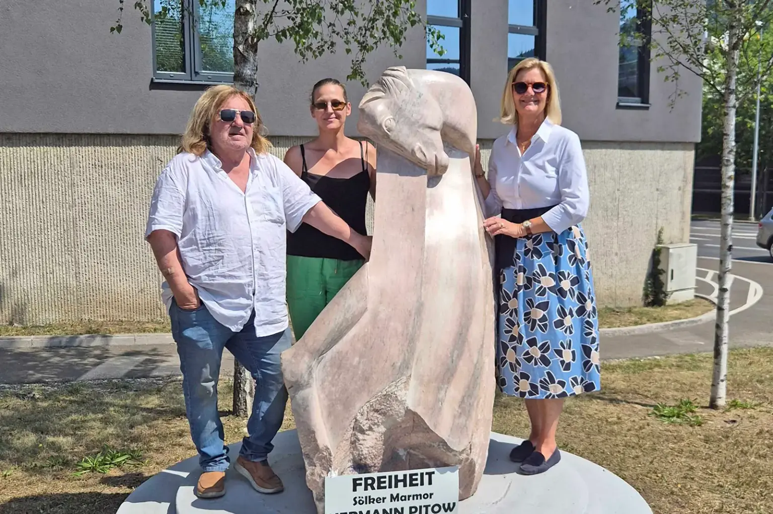 Zwei Frauen und ein Mann stehen an einer Steinskulptur mit Pferdekopf