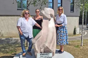 Zwei Frauen und ein Mann stehen an einer Steinskulptur mit Pferdekopf