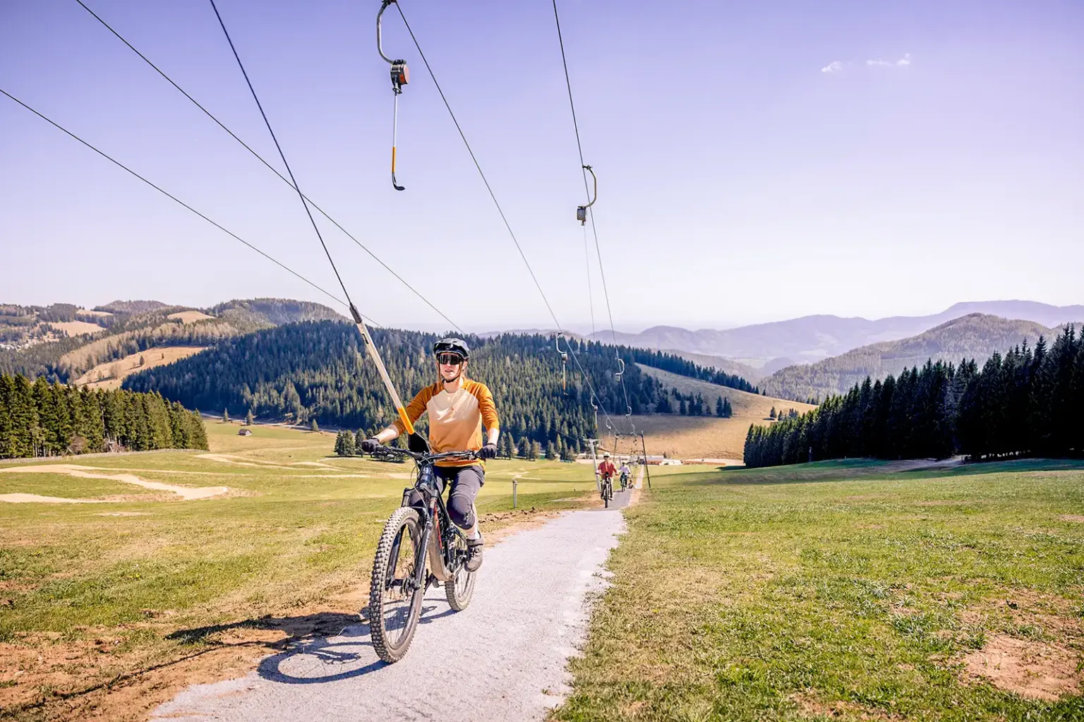 Eine Frau auf einem Mountainbike wird von einem Schlepplift bergwärts gezogen