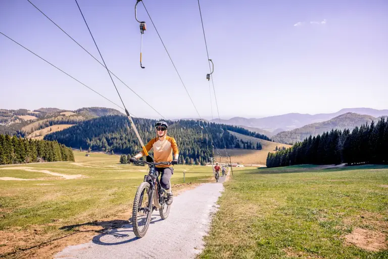 Eine Frau auf einem Mountainbike wird von einem Schlepplift bergwärts gezogen