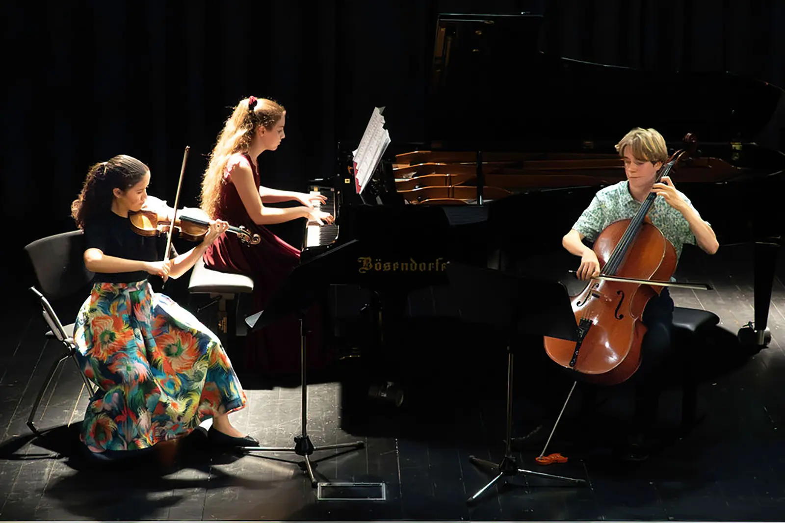 Drei Jugendliche spielen Klavier, Geige und Cello auf einer Bühne