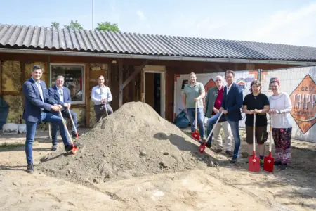 Acht Personen stehen mit roten Spaten rund um einen Sandhaufen vor dem Gebäude des Tierheims Kapfenberg und markieren gemeinsam den symbolischen Spatenstich für den Umbau. Im Hintergrund sind Bauzäune, das sanierungsbedürftige Gebäude und Baustelleneinrichtungen zu sehen.