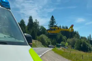 Ein gelber Hubschrauber hebt ab, im Vordergrund die Motorhaube eins Rettungsfahrzeugs