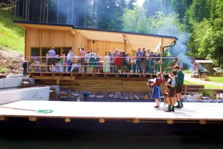 Drei junge MusikerInnen in Tracht spielen auf einem Steg vor einer Holzterrasse