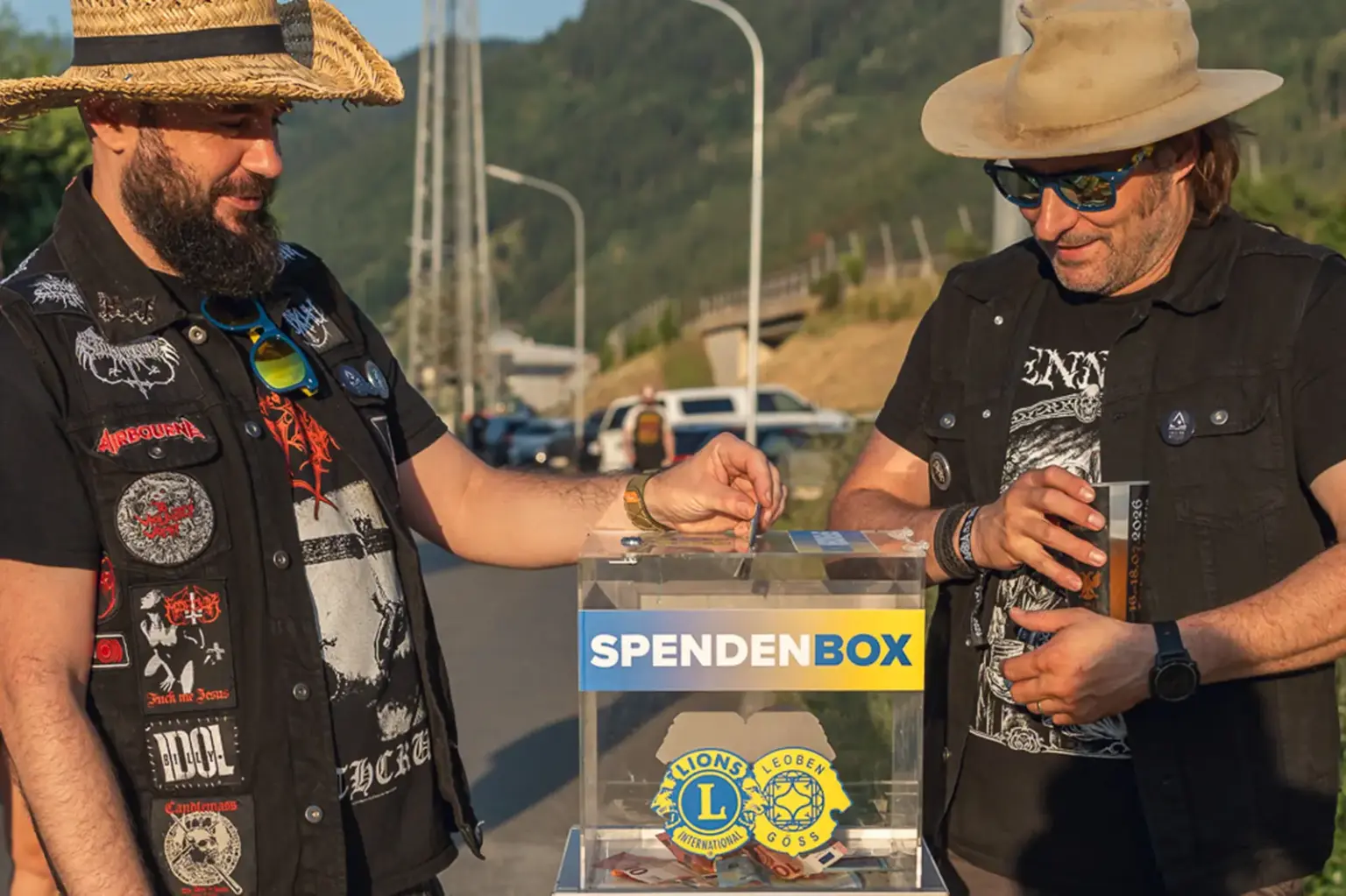 Zwei Männer mit Strohhut und Sonnenbrille werfen Geld in eine Spendenbox