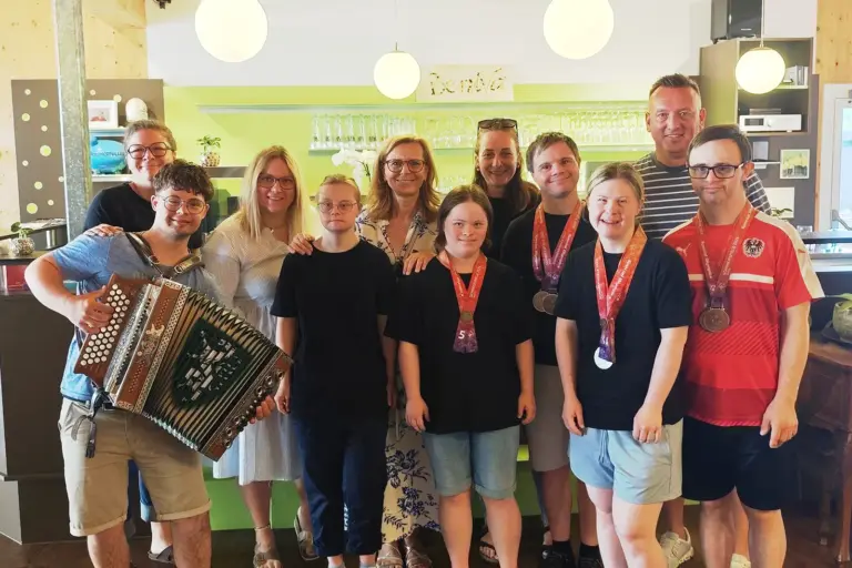 Leobener Beniva-Team gewann neun Medaillen Eine Gruppe aus Jugendlichen und Erwachsenen steht gemeinsam in einem Café und lächelt in die Kamera. Mehrere Personen tragen Medaillen um den Hals, eine Person im Vordergrund hält eine steirische Harmonika.