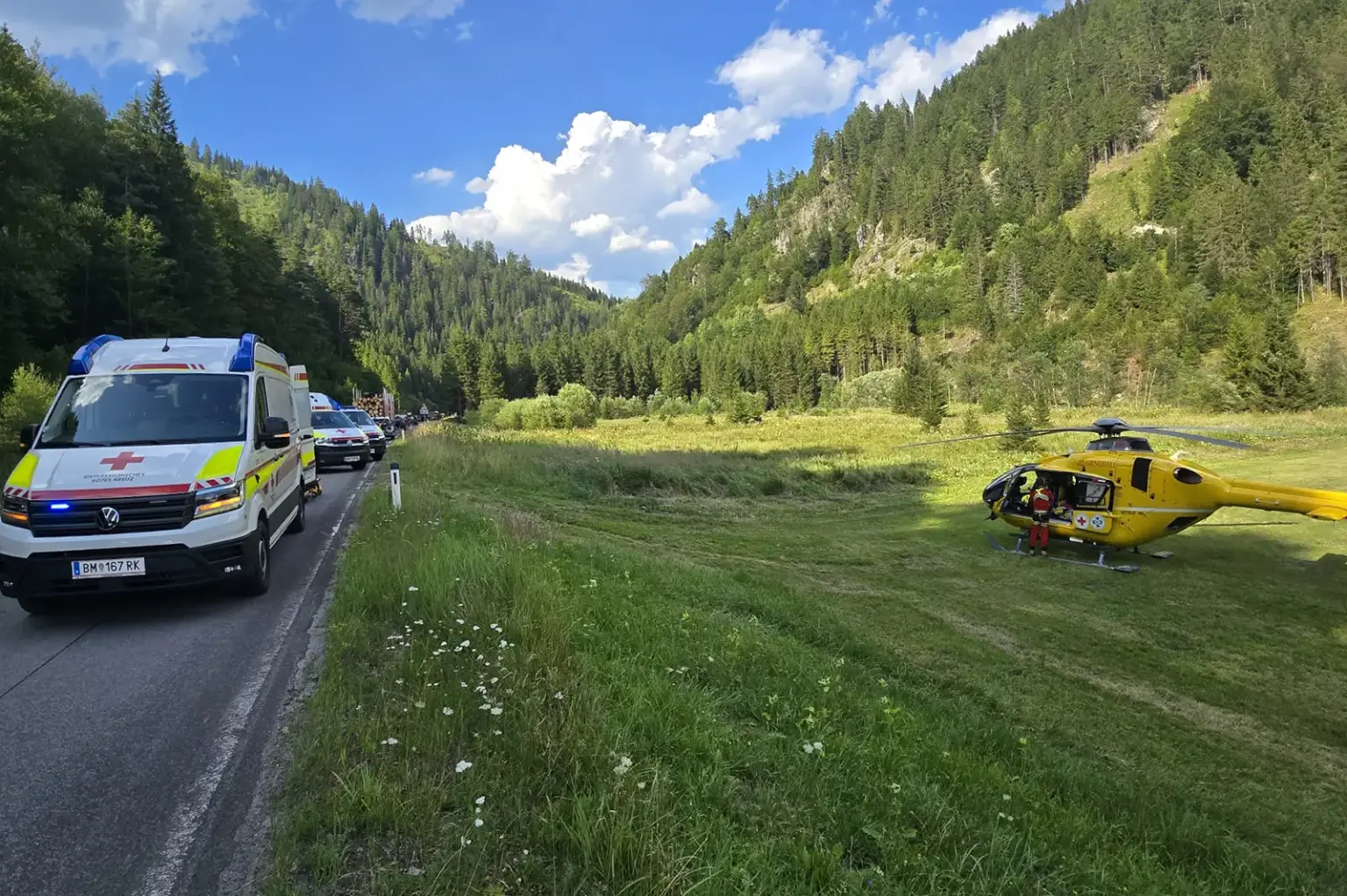 Zwei Unfälle im Mariazellerland Ein gelber Hubschrauber steht auf einer Wiese neben einer Straße mit mehreren Rettungsfahrzeugen
