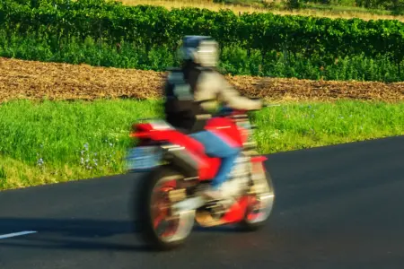 Ein Motorrad fährt auf einer Landstraße von links nach rechts, aufgrund der Bewegung erscheint das Fahrzeug unscharf