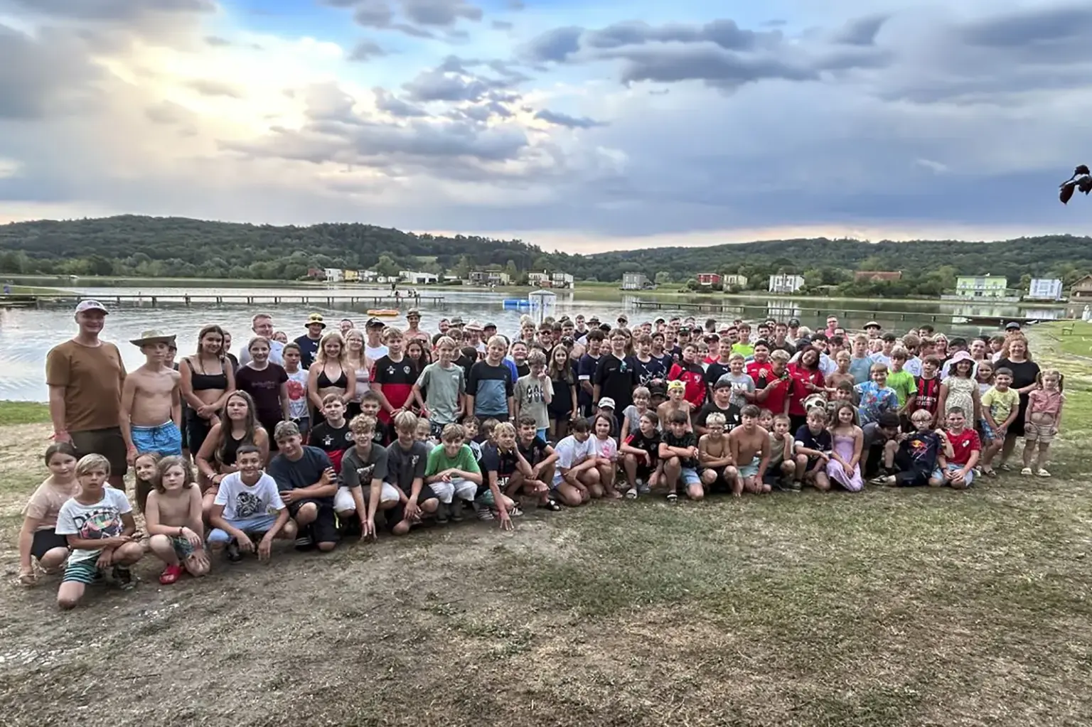 Eine große Gruppe von Jugendlichen posiert auf einer Wiese vor einem See