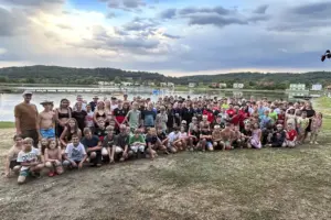 Eine große Gruppe von Jugendlichen posiert auf einer Wiese vor einem See