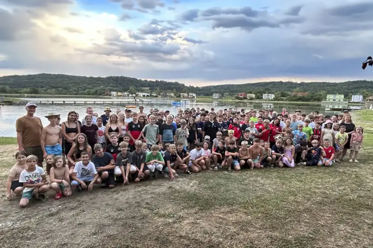 Eine große Gruppe von Jugendlichen posiert auf einer Wiese vor einem See
