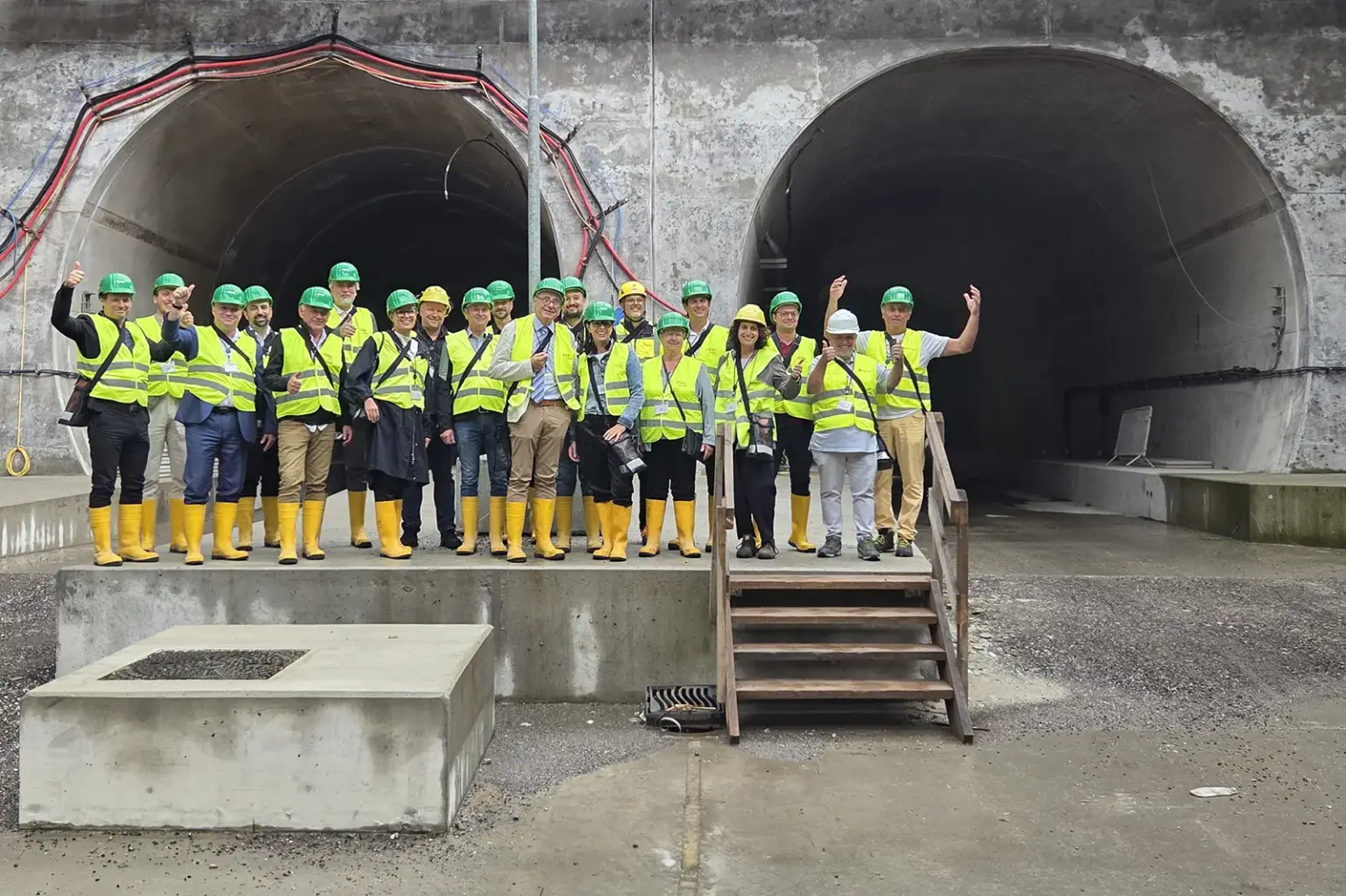 Eine Gruppe von Personen in Warnwesten und Helmen steht vor zwei Tunnelportalen