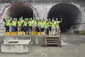 Eine Gruppe von Personen in Warnwesten und Helmen steht vor zwei Tunnelportalen
