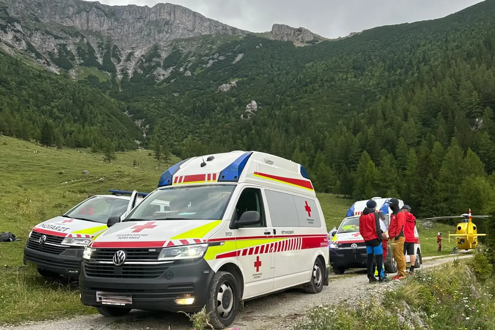 Drei Rettungsfahrzeuge, ein Hubschrauber und Rettungskräfte vor einem felsigen Berghang