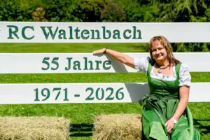 Eine Frau in Trachtenkleidung sitzt auf einem Strohballen an einem Springreit-Hindernis