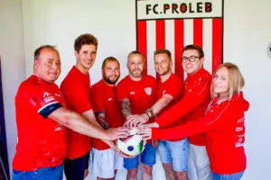 Sechs Männer und eine Frau halten gemeinsam einen Fußball