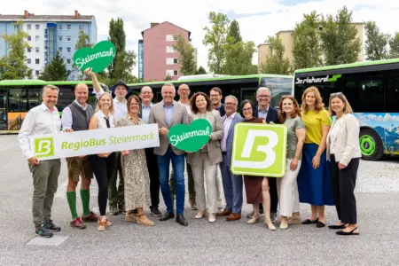 Schöner fahren: Steirische Regionen zieren Linienbusse Eine Gruppe von zirka 15 Menschen mit Schildern in Händen, im Hintergrund Linienbusse