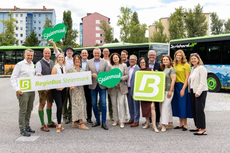 Schöner fahren: Steirische Regionen zieren Linienbusse Eine Gruppe von zirka 15 Menschen mit Schildern in Händen, im Hintergrund Linienbusse