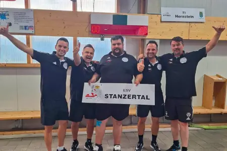 ESV Stanzertal steigt in die Bundesliga auf Fünf Männer in schwarzen Vereinsshirts stehen in einer Stocksporthalle und halten ein Schild mit der Aufschrift „ESV Stanzertal“. Mehrere von ihnen zeigen jubelnd den Daumen nach oben.