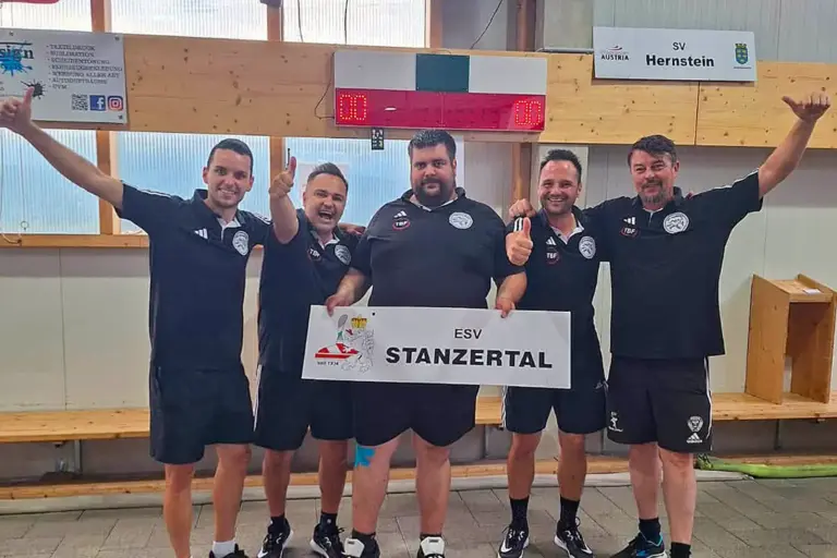 ESV Stanzertal steigt in die Bundesliga auf Fünf Männer in schwarzen Vereinsshirts stehen in einer Stocksporthalle und halten ein Schild mit der Aufschrift „ESV Stanzertal“. Mehrere von ihnen zeigen jubelnd den Daumen nach oben.