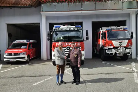 Zwei Männer schütteln sich vor einer Garage mit drei Feuerwehrautos die Hände